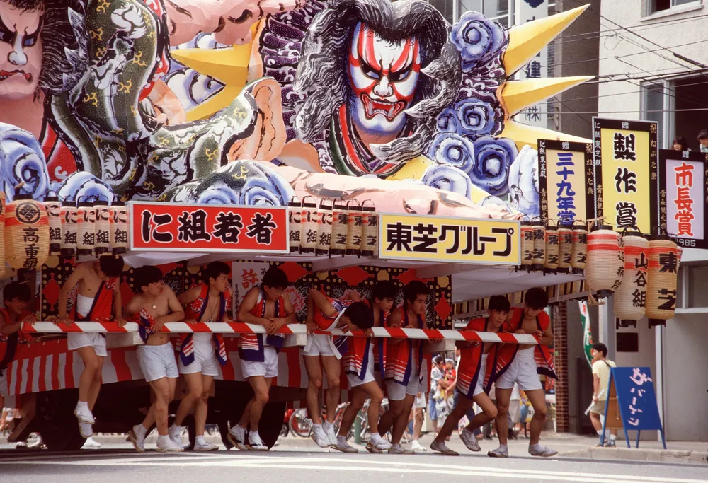 Haneto dancers in traditional costume parade beside a Nebuta float